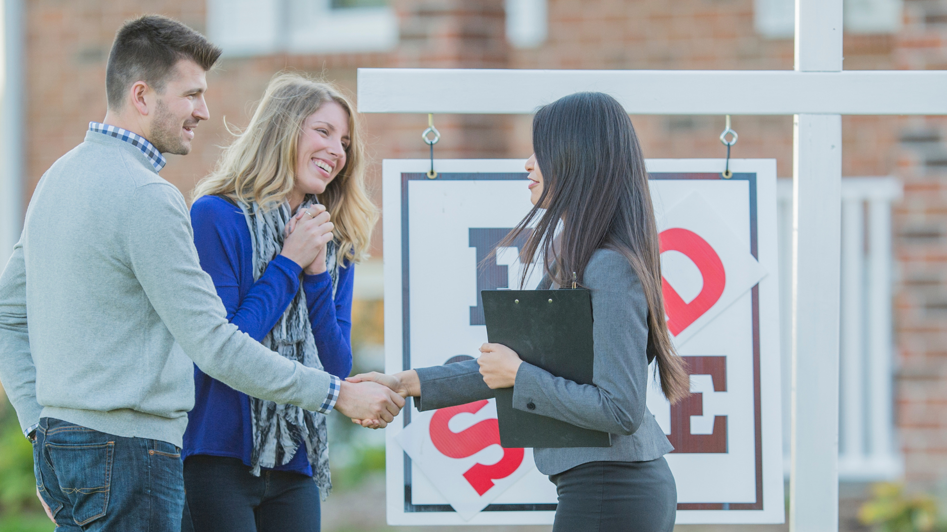 two friends buying a house together with a realtor in front of a "SOLD" sign How to Buy a House With a Friend?