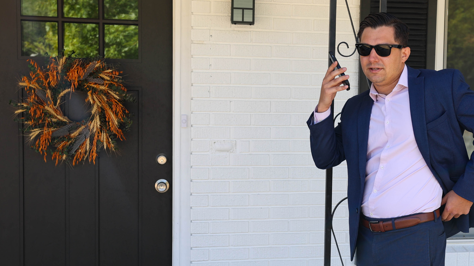 realtor on a phone call in front of a white house with a black door.